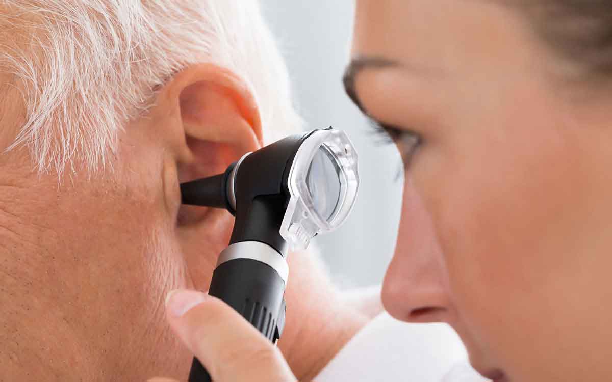 A healthcare professional examines an elderly persons ear using an otoscope, checking for ear health or possible ear issues.