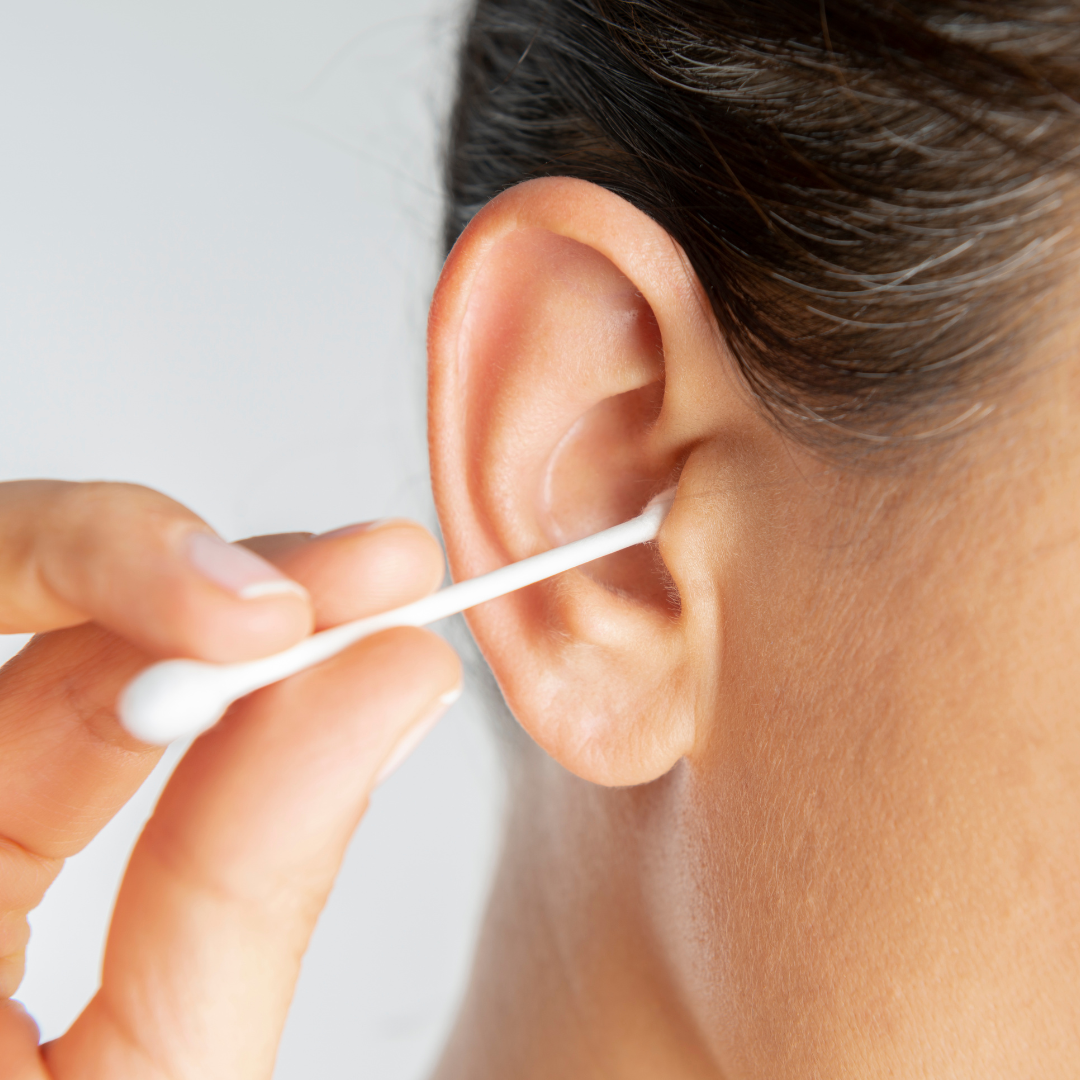 A person cleaning their ear with a cotton swab, close-up view of the ear and hand.